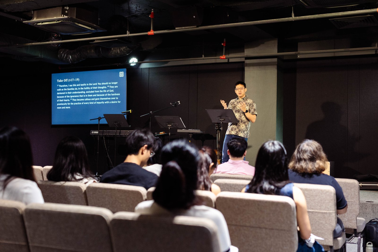 A speaker teaching from a podium in front of a seated congregation during a Sunday morning service.
